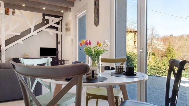 Uma área de refeições com uma mesa redonda, cadeiras, um vaso com flores e vista para o exterior.