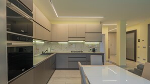 A modern kitchen with a marble countertop, integrated appliances, and a dining area with a white table and chairs.