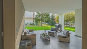A covered patio area with wicker furniture, a glass-top table, and a barbecue grill.