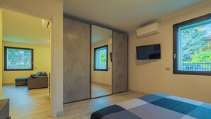 A modern bedroom with a large bed, a wardrobe, a television, and a window with a view of greenery.