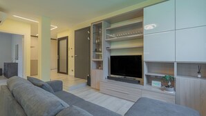 A modern living room with a grey sofa, a flat-screen TV, built-in shelves, and a minimalist design.