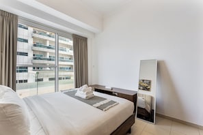 A modern hotel room with a large bed, a bedside table, a mirror, and a view of a high-rise building through floor-to-ceiling windows. - Chic 1BR APT in Business Bay Close To Burj Khalifa (Dubai)