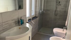 A modern bathroom with a large bathtub, a separate toilet, and a glass-enclosed shower area.