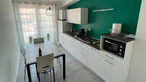 A modern kitchen with white cabinets, a green accent wall, a dining area with a table and chairs, and a built-in microwave.