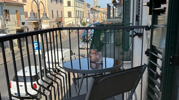A balcony with a table and chair, overlooking a street with parked cars and buildings.