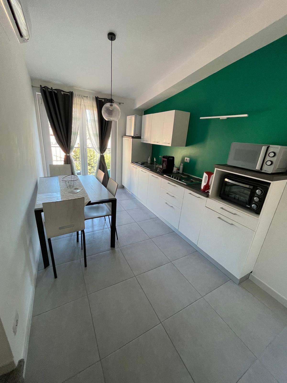 A compact kitchen with white cabinets, a dining table with chairs, and a green accent wall.