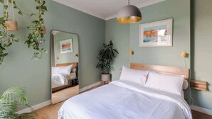 Ein Schlafzimmer mit einem Bett, einem Spiegel, einer hängenden Pflanze, einer Topfpflanze und einem Bild an der Wand.