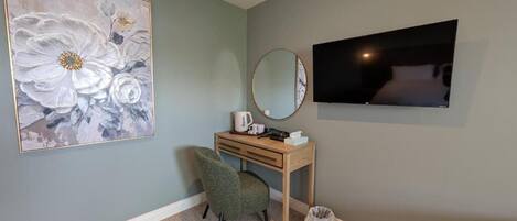 A room with a large floral painting, a desk with a mirror, a television, and a chair.