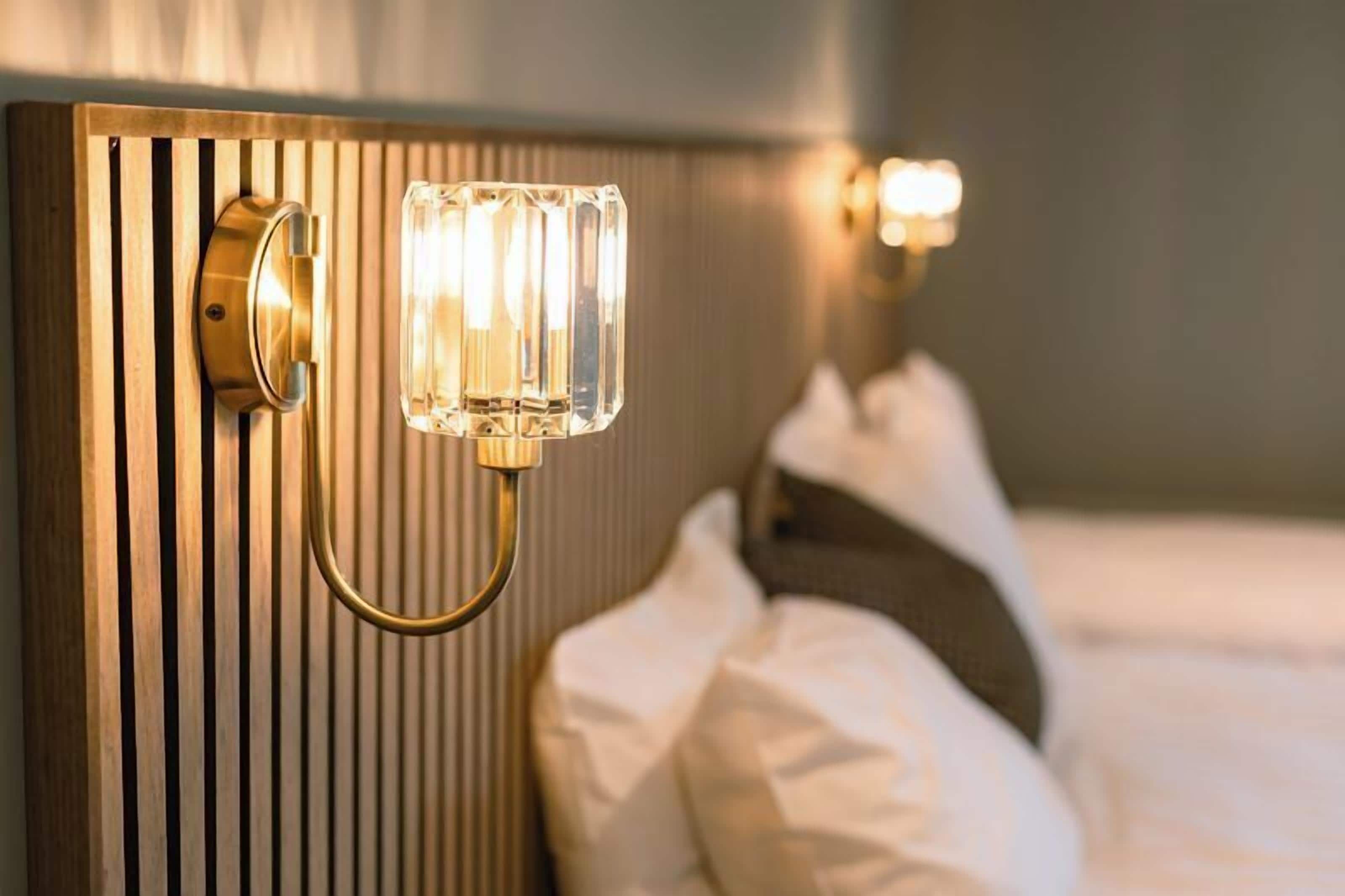 A hotel room with a wooden headboard, a bedside lamp, and a bed with white bedding.