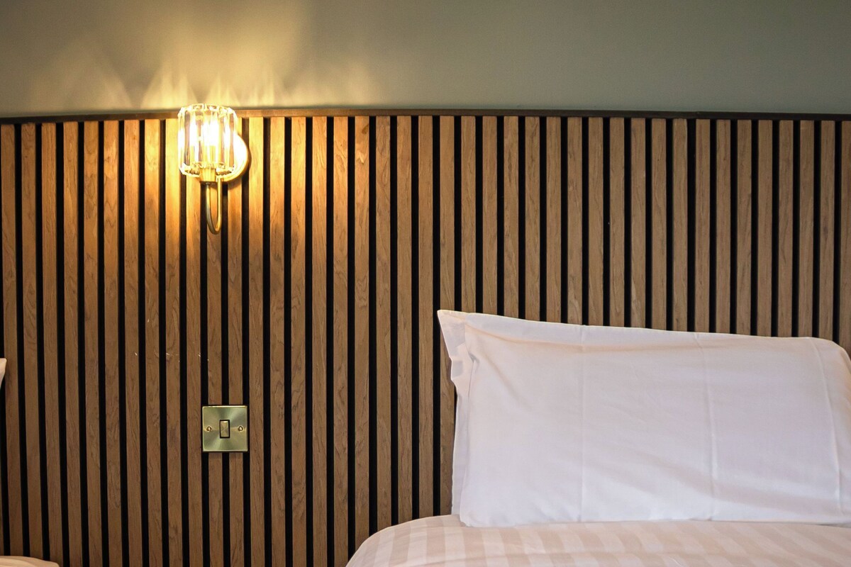 Hotellihuone, jossa on puinen pääty, yöpöytä, jossa on yksi laatikko, ja valkoisilla vuodevaatteilla varustettu sänky.
