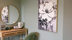 Ein Zimmer mit einem Holztisch, einem grünen Stuhl, einem runden Spiegel und einem großen Blumenbild an der Wand.