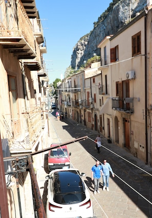 Une rue étroite, bordée de bâtiments des deux côtés, avec une voiture rouge garée à gauche et une voiture blanche au milieu.
