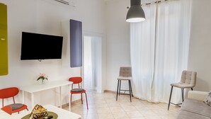 A modern living room with a flat-screen TV, a dining table, two chairs, a sofa, and a large window with curtains.
