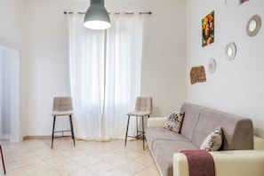 A living room with a sofa, two chairs, a hanging light, a curtain, and wall decorations. - Apartment 'Appartamento Speranza' with Wi-Fi and Air Conditioning (Grosseto)