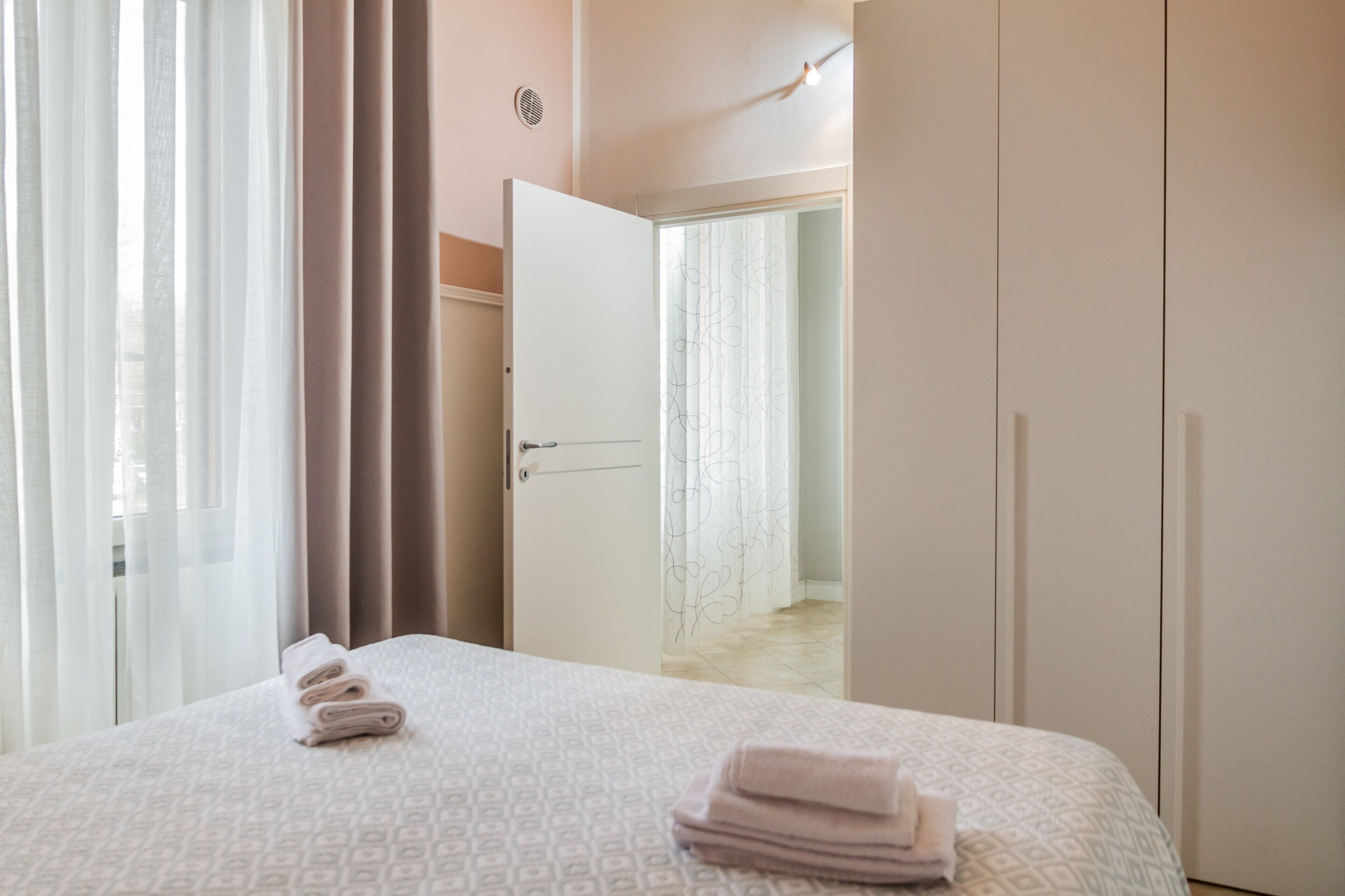 Ett hotellrum med en säng, en dörr som leder till ett annat rum och ett fönster med gardiner.