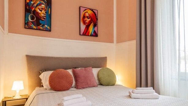 A hotel room with a bed, pillows, a nightstand, a lamp, and artwork on the wall.