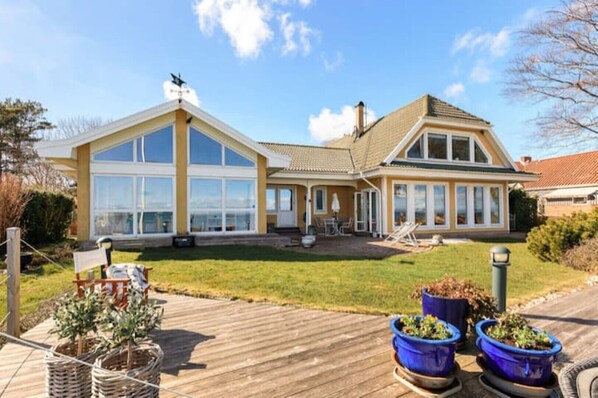 A two-story house with large windows, a deck, and potted plants.