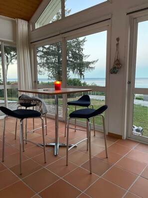 A room with a table and two chairs, a candle on the table, and a view of the outdoors through large windows.