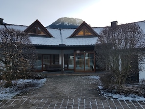 Een gebouw met een met sneeuw bedekte dak, een houten bank en een verharde opgang.
