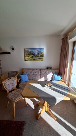 Un salon comprenant un canapé, des fauteuils, une table, une horloge et un tableau représentant un paysage de montagne.