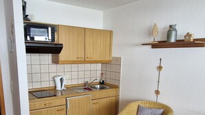 Een kleine keuken met houten kastjes, een inbouwmagnetron, een spoelbak en een kleine koelkast.