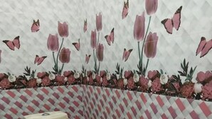 A bathroom with a toilet, a pink bucket, and patterned walls. - Hotel Krishna Inn (Karchana)