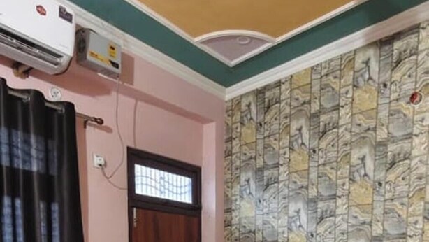 A bedroom with a bed, a ceiling fan, a wall-mounted air conditioner, and a patterned wallpaper. - Hotel Krishna Inn (Karchana)