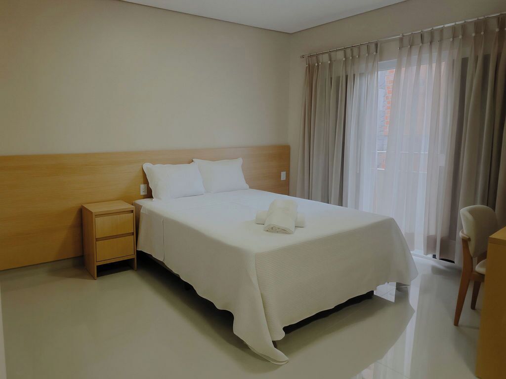 A neatly made bed with a wooden headboard, a bedside table, and a chair.