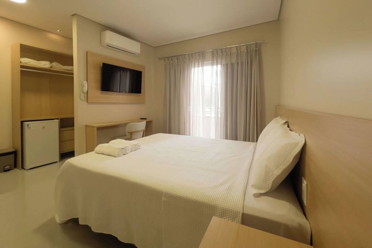 A hotel room with a large bed, a desk, a TV, and a wardrobe.