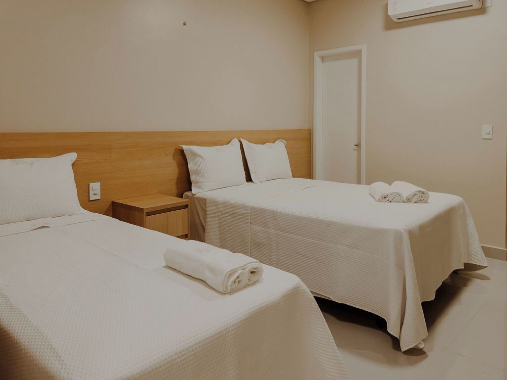 Una habitación de hotel con dos camas, cabecero de madera, una mesita de noche y una puerta.