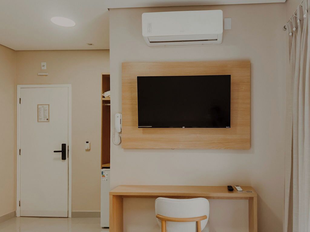 A room with a mounted TV, a desk with a chair, and a door.