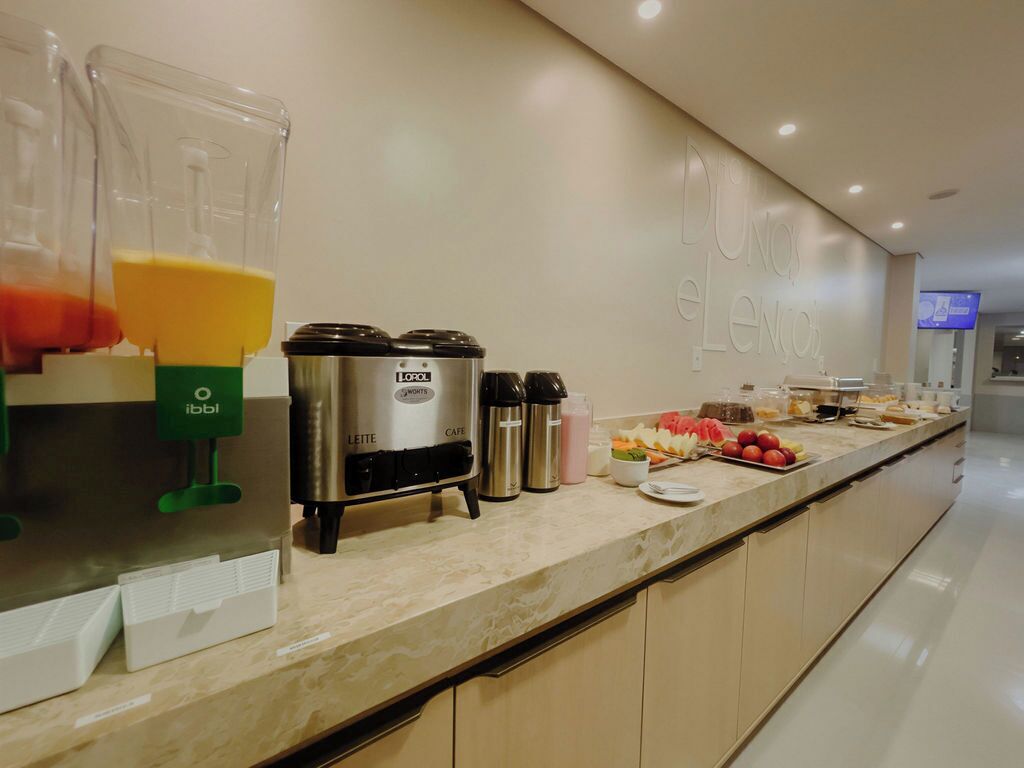 A breakfast bar with a coffee machine, a fruit display, and a wall with the text "Dun E Lenoir".