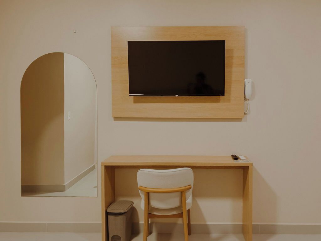 Una habitación con un espejo grande, un televisor de pantalla plana en la pared, un escritorio de madera y una silla blanca.