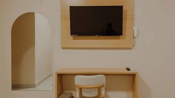 Una habitación con un espejo grande, un televisor de pantalla plana en la pared, un escritorio de madera y una silla blanca.