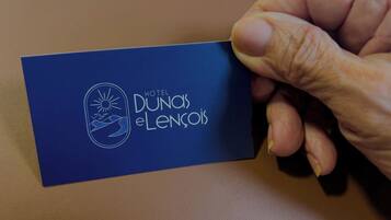 Una mano sostiene una tarjeta de presentación del HOTEL DUNOS ELENCOIS.