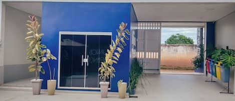 A modern building with a blue facade, a glass door entrance, and potted plants.