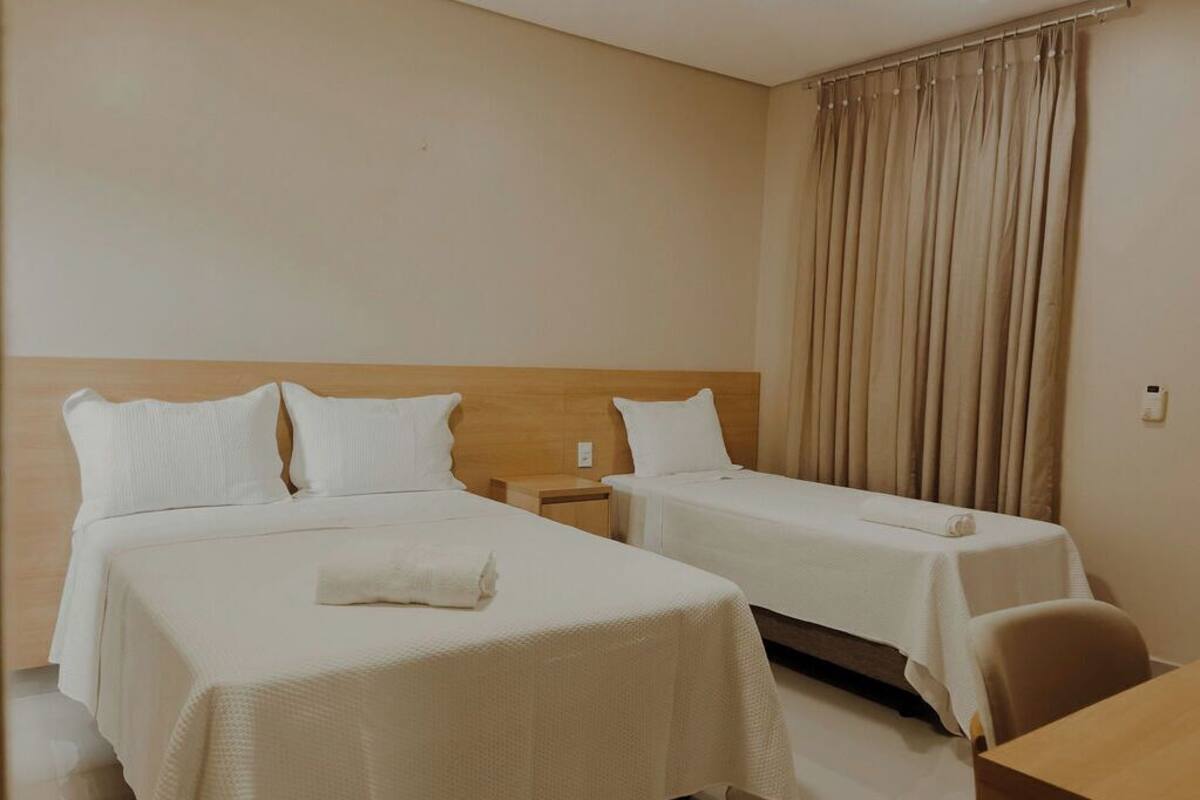 A hotel room with two beds, a wooden headboard, a small table, and a curtain.
