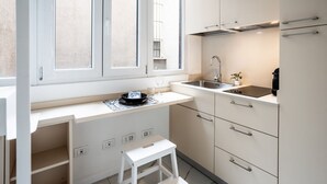 Une cuisine de taille réduite, dotée d’une fenêtre, d’un évier et d’un petit tabouret.