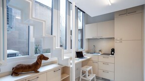 Une cuisine moderne avec des meubles blancs, un ordinateur portable posé sur un bureau blanc et un petit tabouret blanc.