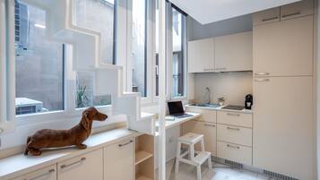 Une cuisine moderne avec des meubles blancs, un ordinateur portable posé sur un bureau blanc et un petit tabouret blanc.