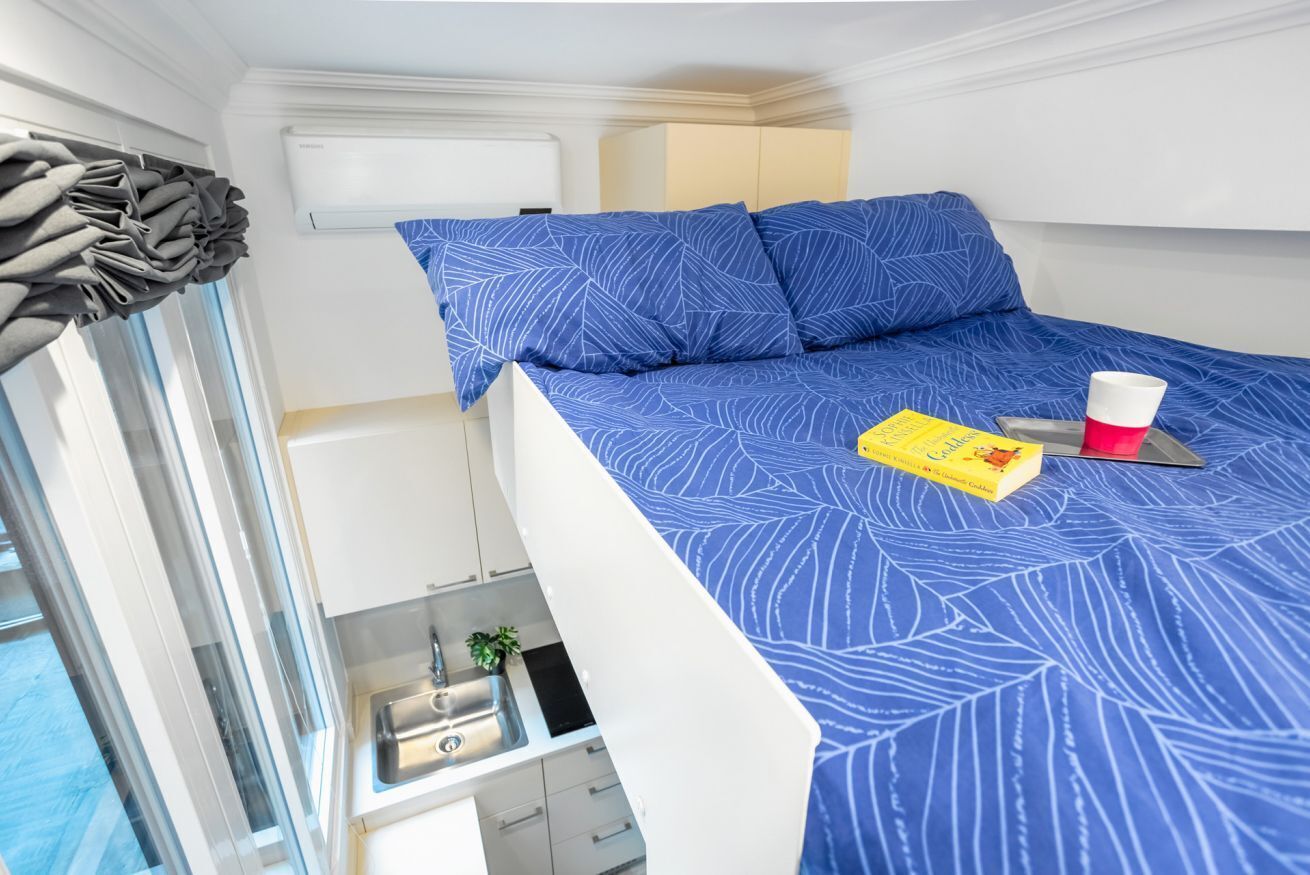 Une petite pièce comprenant un lit superposé, un coin cuisine et une fenêtre avec des rideaux.