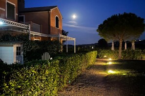 A building with a covered porch, a tree, and a pathway lit by ground lights. - P079 - Porto Recanati, two-room apartment with courtyard in a residence with pool. (Porto Recanati)