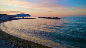 A beach with calm water, a distant mountain, and a clear sky.