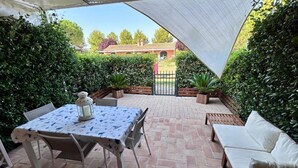 An outdoor patio with a table and chairs, a white sofa, and a view of a building in the background.