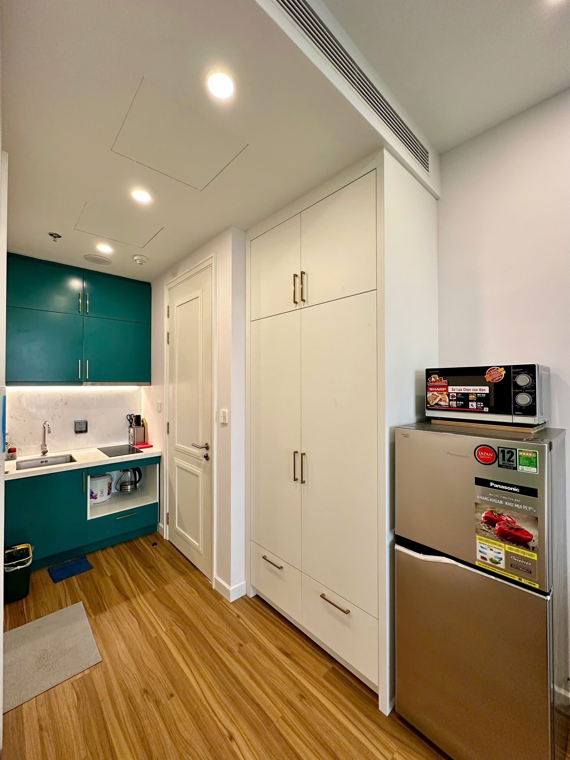 A kitchen with teal cabinets, white doors, a stainless steel refrigerator, and a microwave.