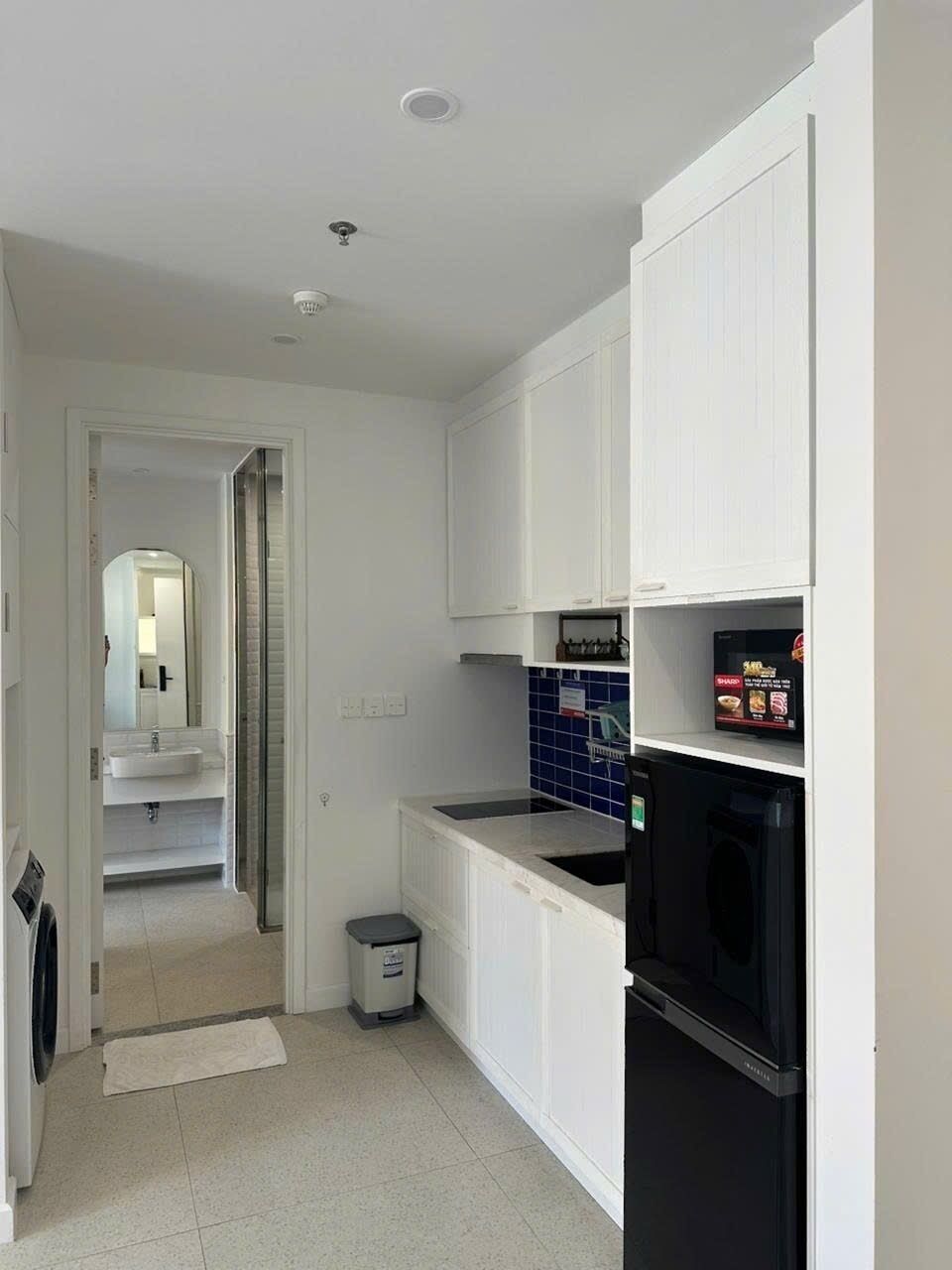 Eine kompakte Küche mit weißen Schränken, einem schwarzen Kühlschrank und einer blauen Fliesenrückwand.
