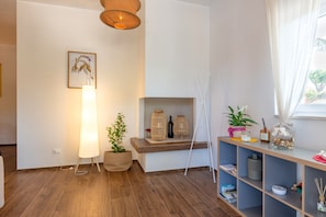 Une chambre moderne avec un plancher en bois, un lampadaire, une plante en pot, une étagère ornée d’objets décoratifs et une fenêtre avec des rideaux.