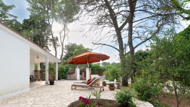 Un patio con piso de piedra, una silla de descanso, un paraguas y plantas en macetas.