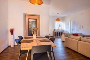 Un soggiorno moderno con zona pranzo, divano e cucina sullo sfondo.