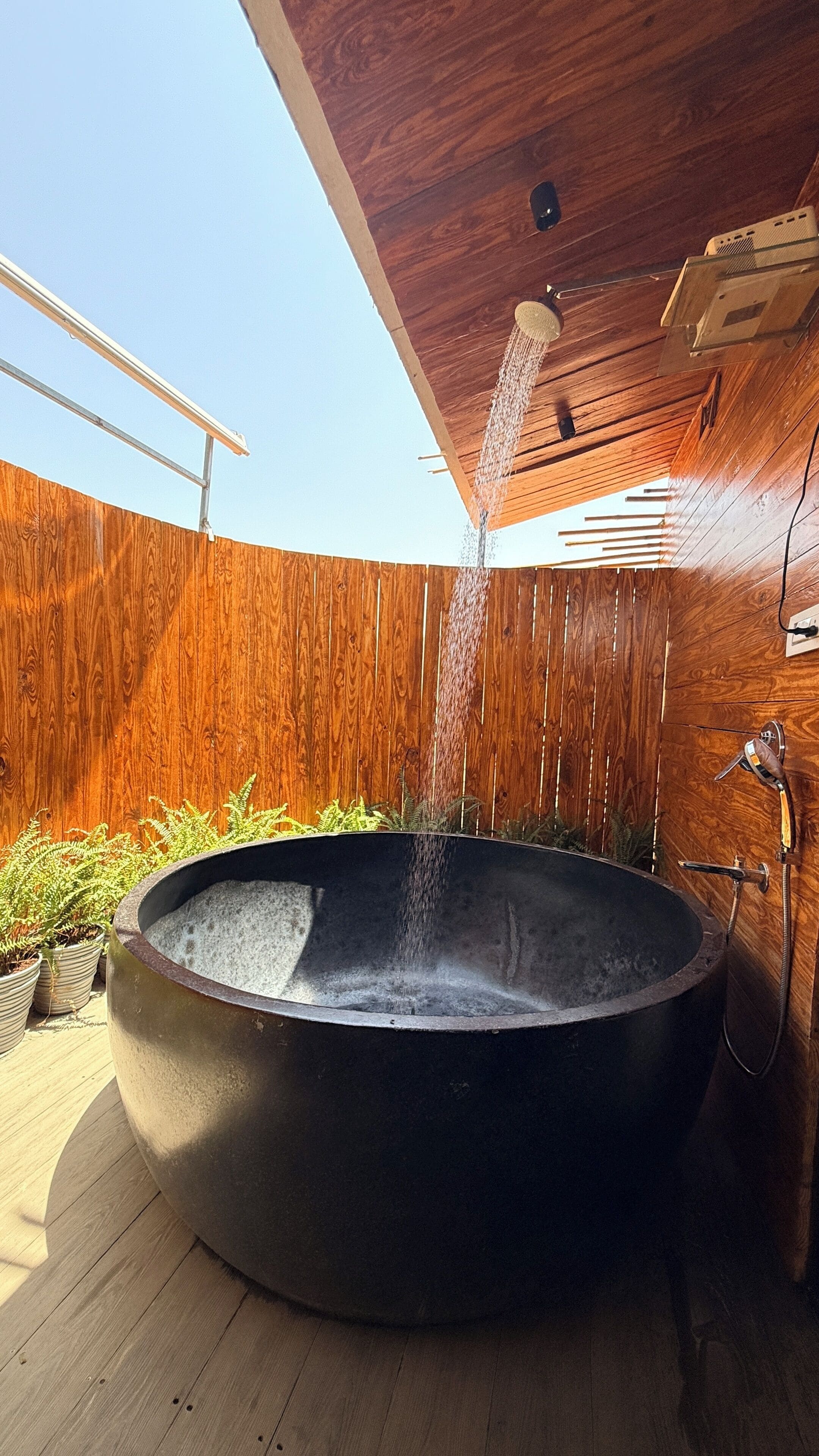 A hot tub with a wooden deck, surrounded by plants, and a wooden fence.